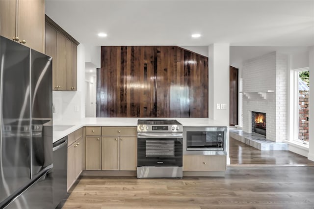 kitchen with a brick fireplace, light hardwood / wood-style flooring, light brown cabinets, kitchen peninsula, and stainless steel appliances