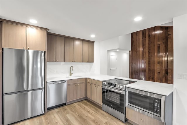 kitchen featuring appliances with stainless steel finishes, kitchen peninsula, sink, and light wood-type flooring