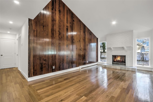 unfurnished living room featuring wood-type flooring, wood walls, a fireplace, and a baseboard radiator