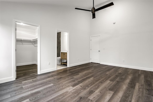 unfurnished bedroom featuring connected bathroom, a walk in closet, dark hardwood / wood-style flooring, a closet, and a towering ceiling