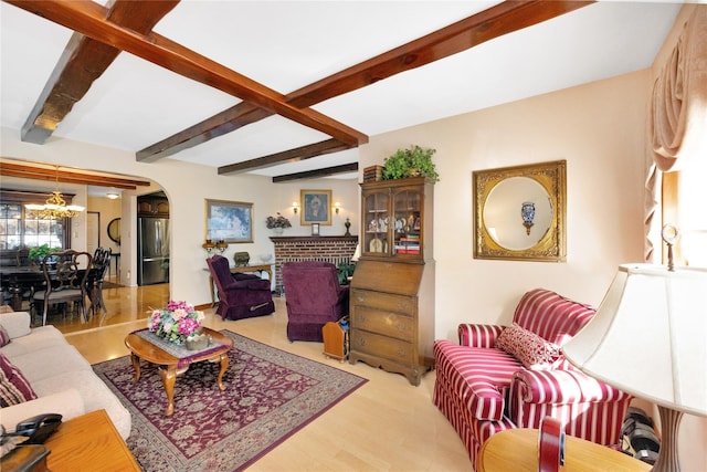 living room with light wood-type flooring, a chandelier, a fireplace, and beamed ceiling