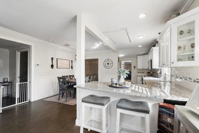 kitchen featuring light stone counters, kitchen peninsula, a breakfast bar area, and white cabinets