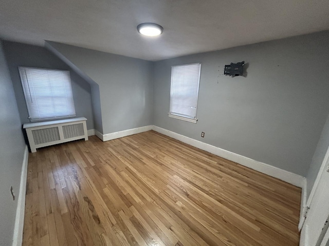 additional living space featuring light wood-type flooring and radiator heating unit