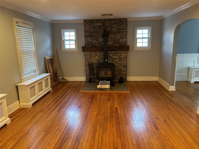 unfurnished living room featuring plenty of natural light, ornamental molding, a wood stove, and hardwood / wood-style floors