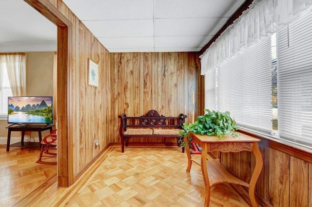 living area with a paneled ceiling, light parquet flooring, plenty of natural light, and wood walls