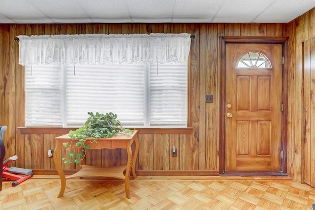 foyer entrance featuring plenty of natural light, a drop ceiling, and wood walls