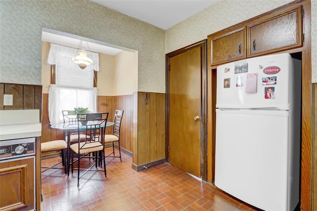 kitchen with hanging light fixtures, wood walls, and white fridge