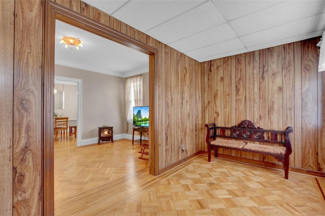 living area with a drop ceiling, wooden walls, and baseboards