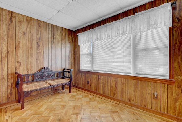 living area featuring a paneled ceiling, wooden walls, and baseboards