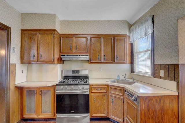 kitchen with stainless steel range with gas cooktop, light countertops, a sink, under cabinet range hood, and wallpapered walls