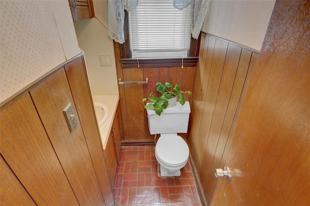 bathroom with toilet, wood walls, brick floor, and vanity