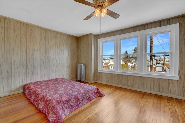 bedroom with baseboards, ceiling fan, hardwood / wood-style flooring, and radiator