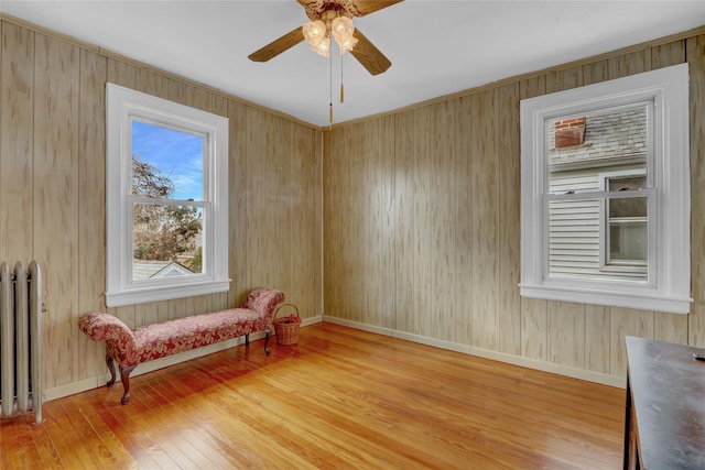 living area featuring a ceiling fan, radiator, light wood-style flooring, and baseboards