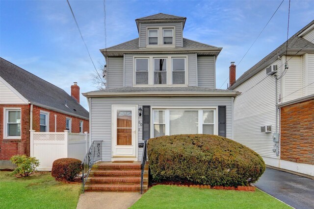 traditional style home with a front yard, a wall mounted air conditioner, roof with shingles, and fence