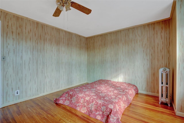 bedroom with radiator heating unit, baseboards, ceiling fan, and wood finished floors