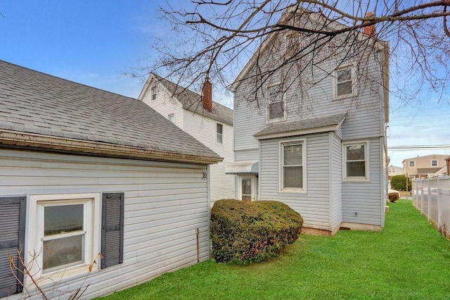 back of house with roof with shingles, a lawn, and fence