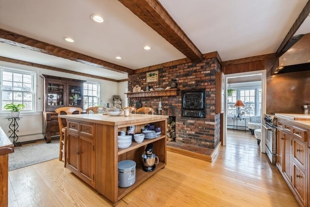 kitchen featuring wall chimney range hood, high end range, a center island, beamed ceiling, and light hardwood / wood-style flooring