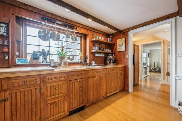 bar featuring light wood-type flooring, beam ceiling, wood walls, and sink