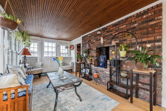 living room featuring light hardwood / wood-style floors, a wood stove, brick wall, and wood ceiling