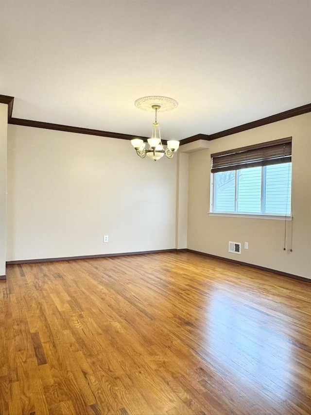 empty room with ornamental molding, light wood-type flooring, and an inviting chandelier