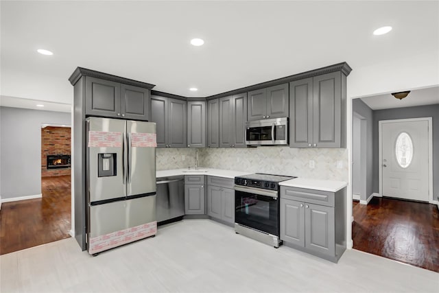 kitchen featuring light hardwood / wood-style floors, gray cabinets, appliances with stainless steel finishes, tasteful backsplash, and a fireplace