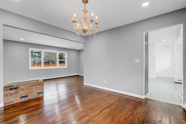 spare room featuring baseboard heating, hardwood / wood-style floors, and a chandelier