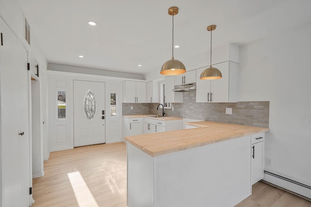 kitchen with a baseboard heating unit, pendant lighting, kitchen peninsula, sink, and white cabinets