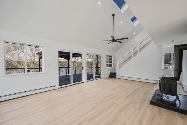 unfurnished living room featuring a skylight, ceiling fan, a wood stove, a baseboard radiator, and light hardwood / wood-style flooring