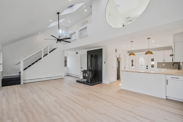 unfurnished living room with baseboard heating, a skylight, a wood stove, and ceiling fan