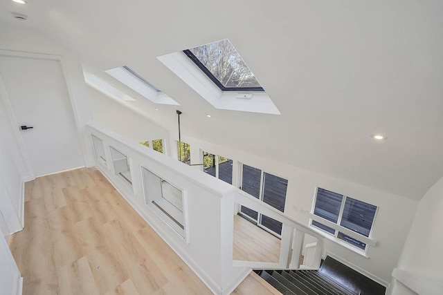 interior space with vaulted ceiling with skylight and light hardwood / wood-style floors