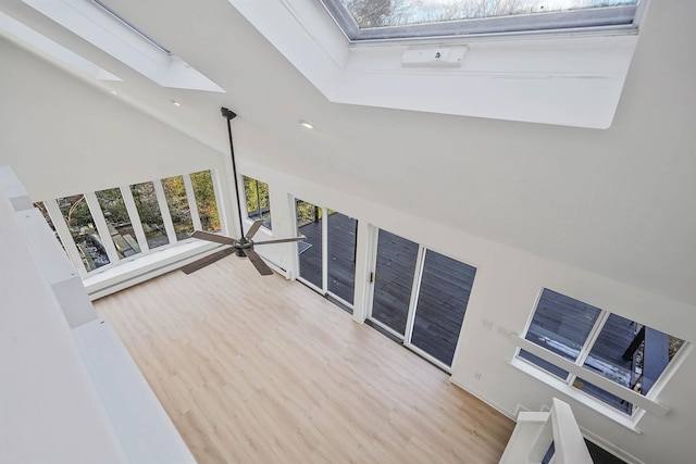 interior space with ceiling fan, hardwood / wood-style floors, high vaulted ceiling, and a skylight