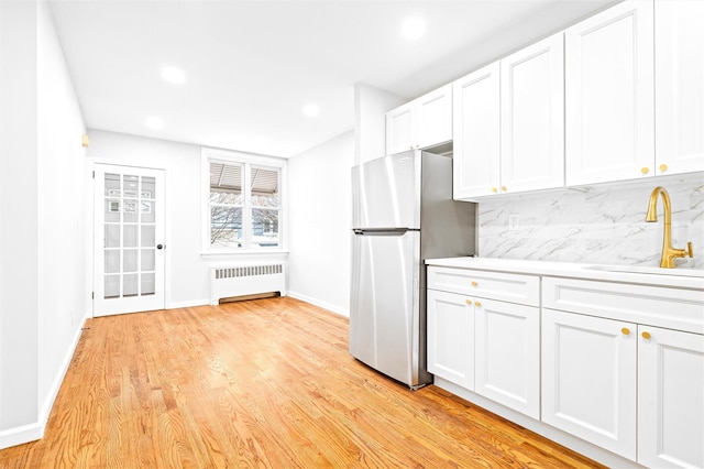 kitchen featuring sink, stainless steel fridge, backsplash, radiator heating unit, and white cabinets