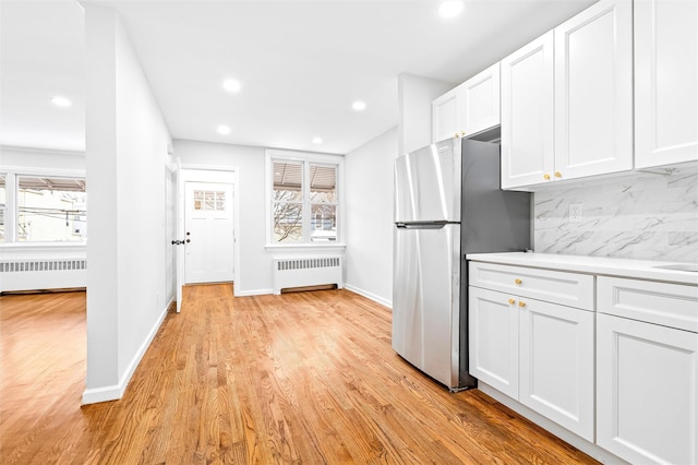 kitchen with stainless steel refrigerator, radiator heating unit, backsplash, and white cabinets