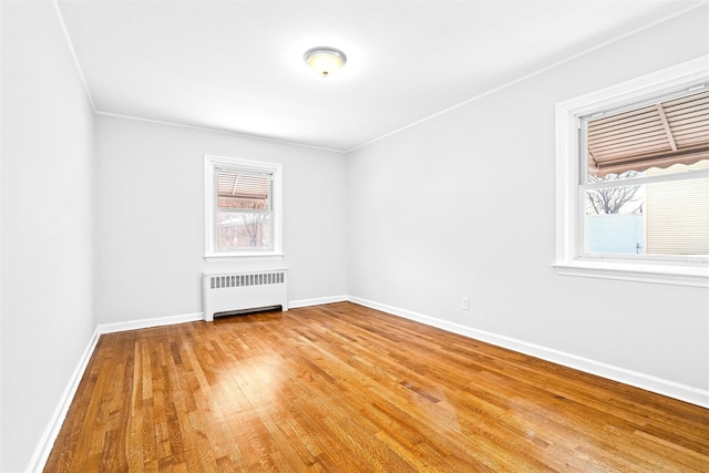 empty room featuring hardwood / wood-style flooring, crown molding, a healthy amount of sunlight, and radiator heating unit