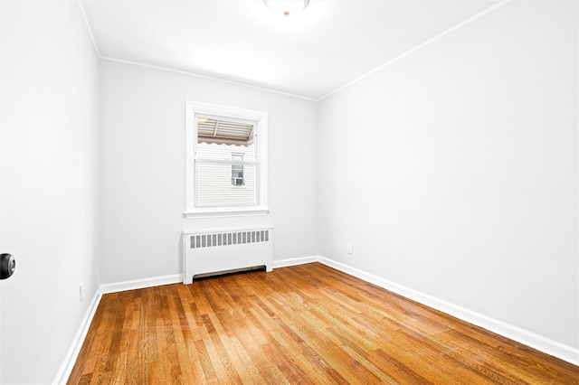 empty room featuring ornamental molding, radiator, and hardwood / wood-style floors