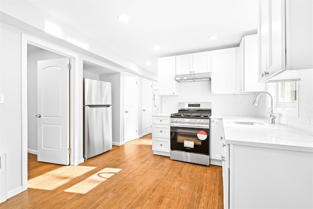 kitchen with sink, stainless steel appliances, light stone countertops, light hardwood / wood-style floors, and white cabinets