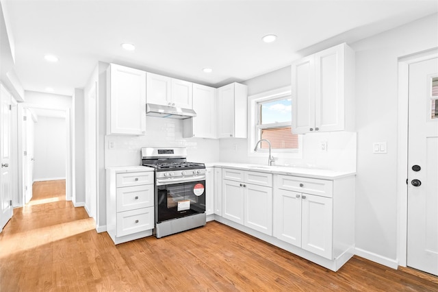 kitchen with white cabinetry, decorative backsplash, stainless steel gas range, and light hardwood / wood-style floors