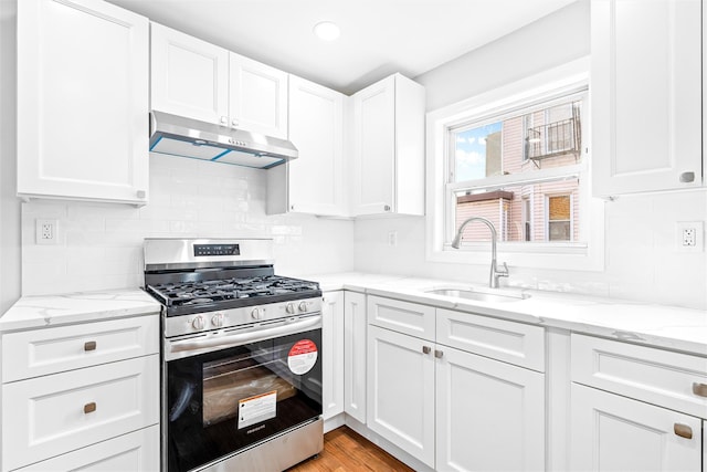 kitchen featuring stainless steel gas stove, sink, white cabinets, light stone counters, and light wood-type flooring