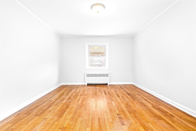 spare room featuring ornamental molding, radiator, and light wood-type flooring