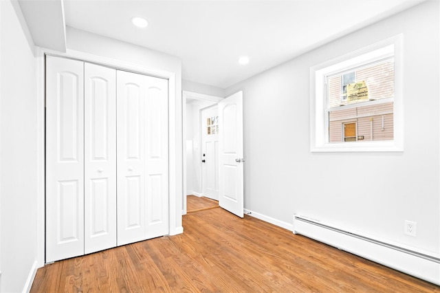 unfurnished bedroom featuring light wood-type flooring, baseboard heating, and a closet