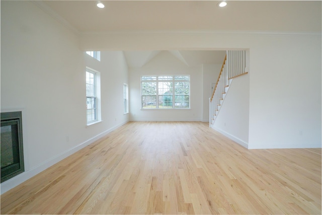 unfurnished living room with a glass covered fireplace, crown molding, baseboards, and light wood-type flooring