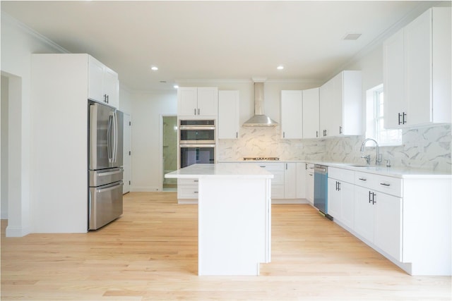 kitchen with a sink, a kitchen island, appliances with stainless steel finishes, crown molding, and wall chimney range hood