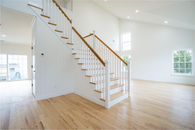 stairs with a towering ceiling, recessed lighting, baseboards, and wood finished floors