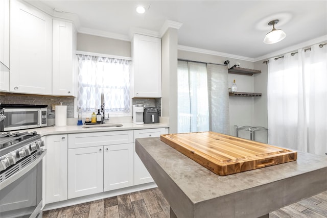 kitchen featuring tasteful backsplash, sink, white cabinets, ornamental molding, and stainless steel appliances