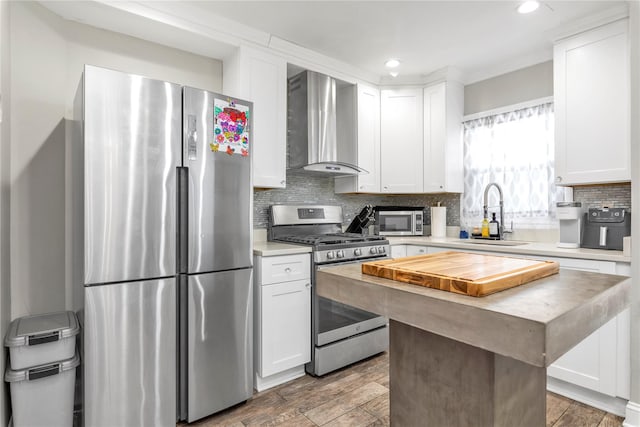 kitchen featuring appliances with stainless steel finishes, wall chimney exhaust hood, sink, and white cabinets