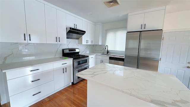 kitchen featuring decorative backsplash, white cabinets, appliances with stainless steel finishes, and light stone countertops