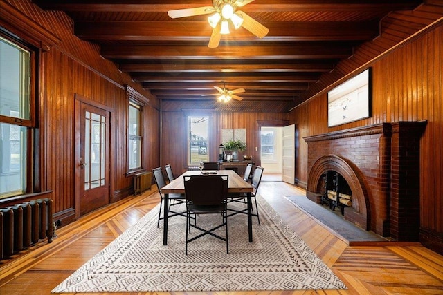 dining room with ceiling fan, wooden walls, radiator, and beam ceiling