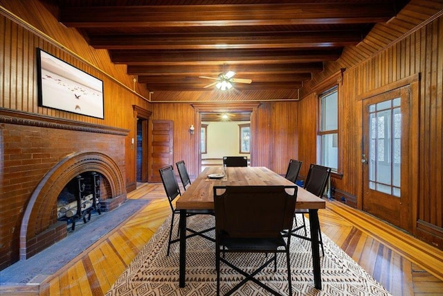 dining room featuring beamed ceiling, a fireplace, and wood walls