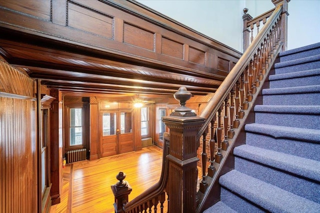 staircase with radiator heating unit, wood ceiling, wooden walls, and hardwood / wood-style flooring