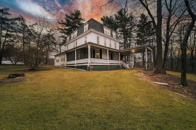 back house at dusk with a sunroom and a lawn